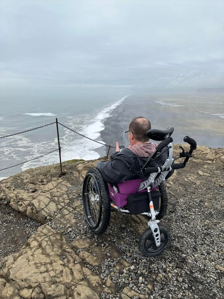 A guest in ILE's all-terrain wheelchair at a black-sand clifftop on Iceland's south coast
